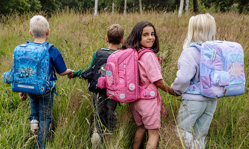 Børn i højt græs med deres nye skoletasker. Få gode råd til at vælge den rigtige skoletaske på neye.dk